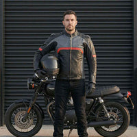 A man in a motorcycle jacket holding a helmet next to a motorcycle.
